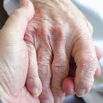 Main d'une personne âgée soutenue par une main soutenante.