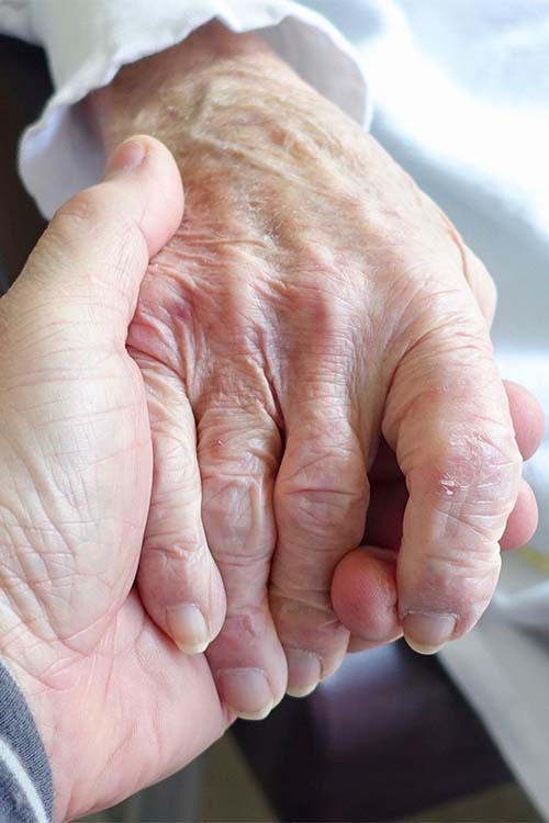 Main d'une personne âgée soutenue par une main soutenante.